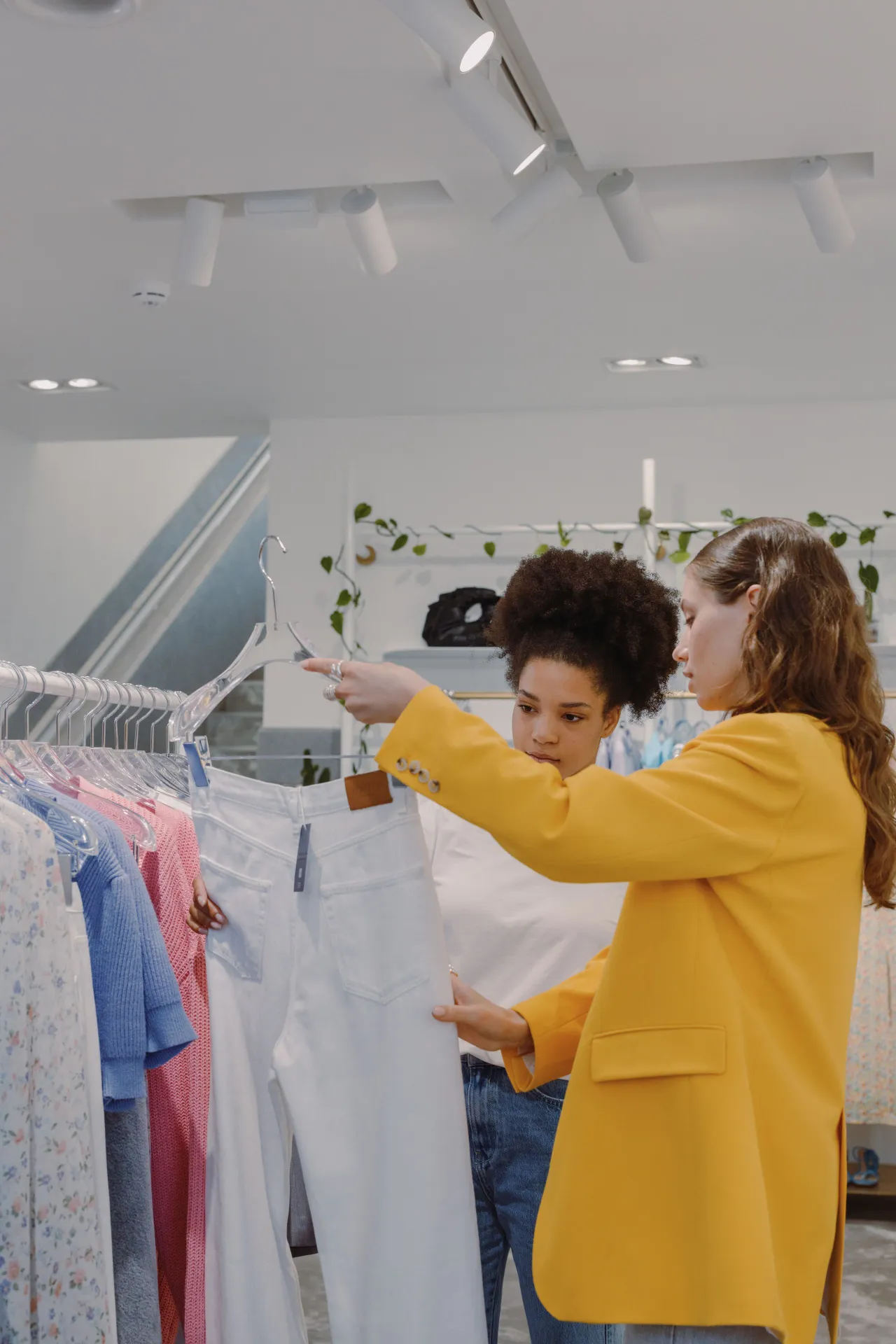Dos personas revisando un perchero de pantalones blancos en una tienda de ropa.